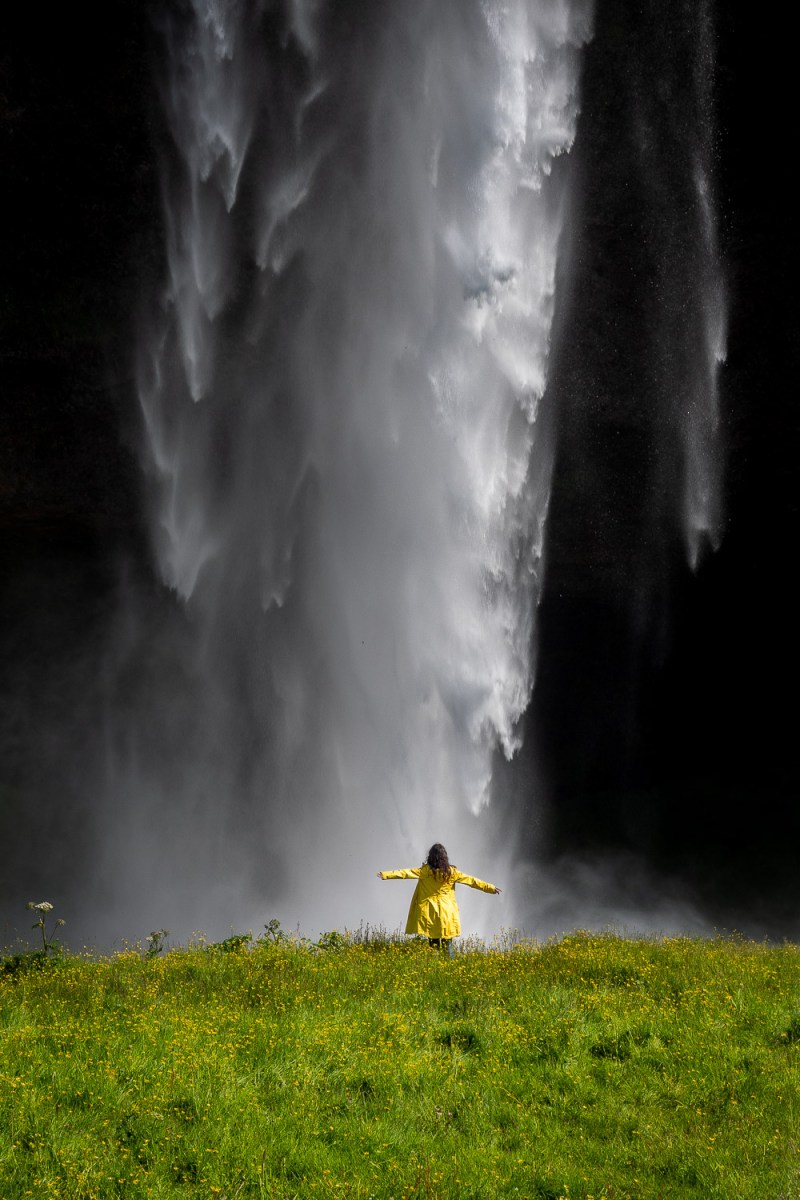 Girl standing under a waterfall, Seljalandfoss, Iceland.